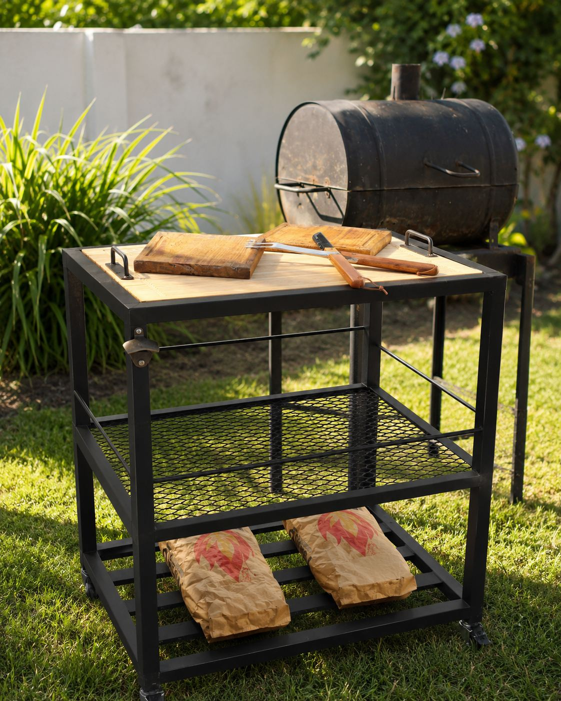 Mesa de Apoyo para Parrillero FORZA KINCHO junto a la parrilla, con tablas, utensilios y bolsas de carbón
